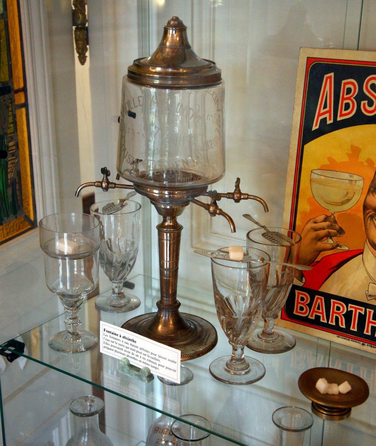 A glass absinthe fountain with several taps and glasses set beneath them