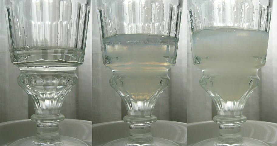 Iced water dripping onto a sugar cube on a slotted spoon as green absinthe clouds to milky white