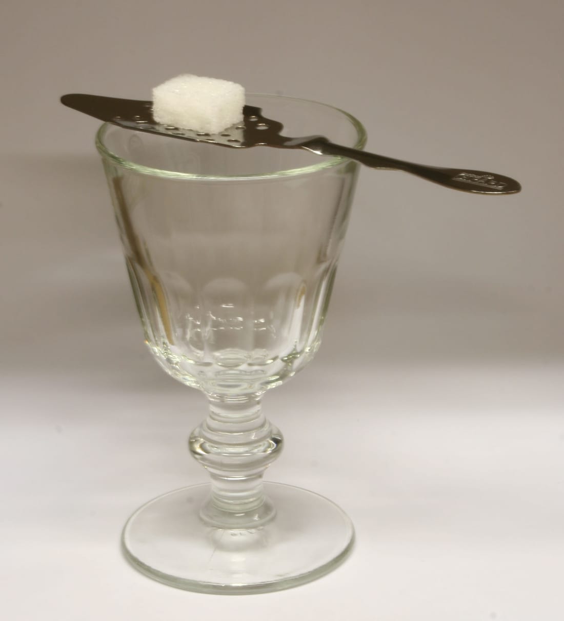 A slotted absinthe spoon laid across a glass with a sugar cube resting on top