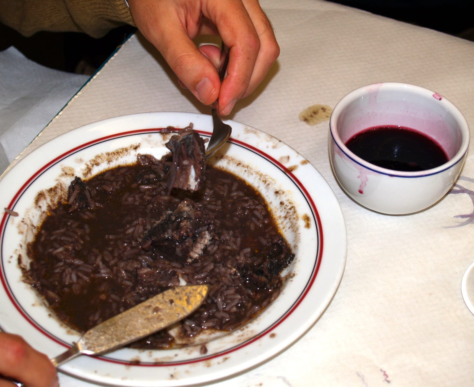 ヤツメウナギのご飯の皿の横で白い碗に注がれた赤のヴィーニョ・ヴェルデ