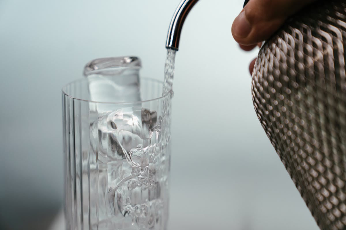 Soda water being poured slowly into a highball glass with ice
