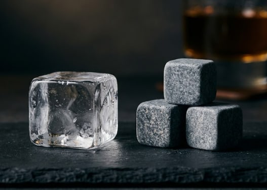 A large ice cube on one side and three whisky stones on the other